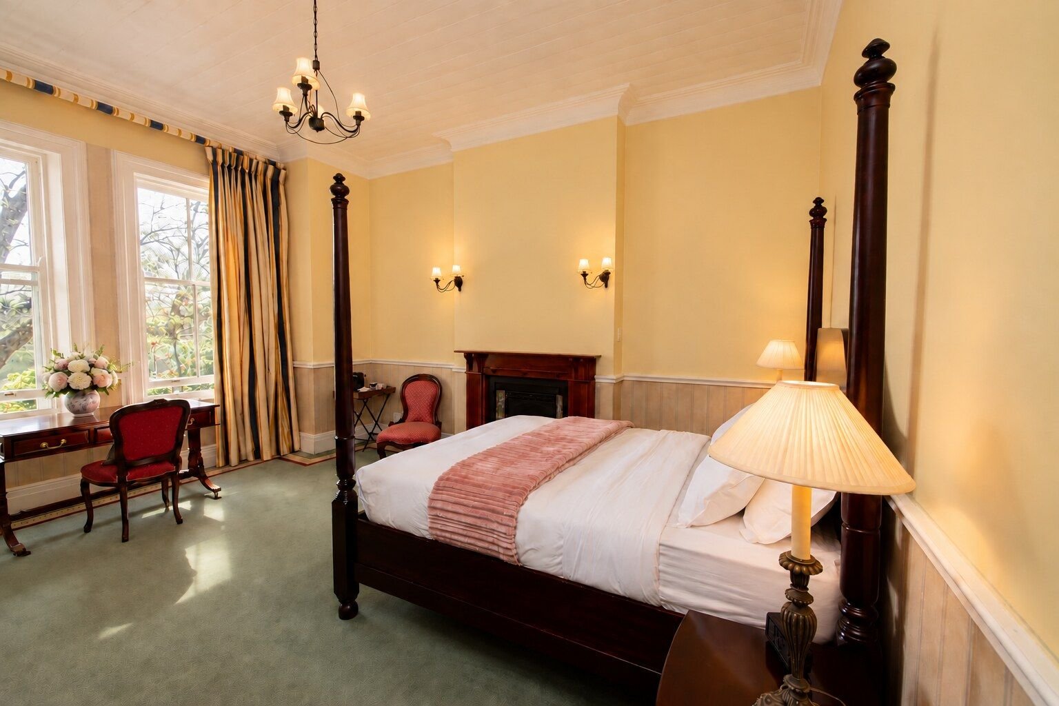 Room IV, Deluxe Queen: butter yellow walls, a four-poster bed and a writing desk by tall sash windows.